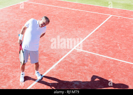 Lunghezza completa di senior man standing con mal di schiena su rosso corte durante il match sulla giornata di sole Foto Stock