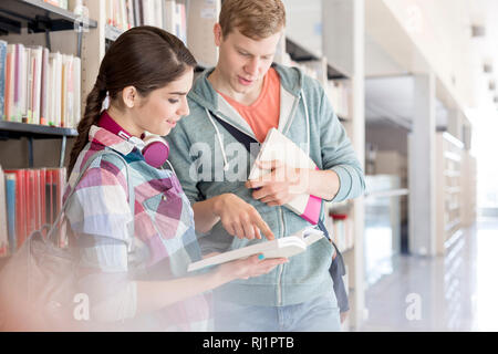 Agli studenti di comunicare con libri in biblioteca universitaria Foto Stock