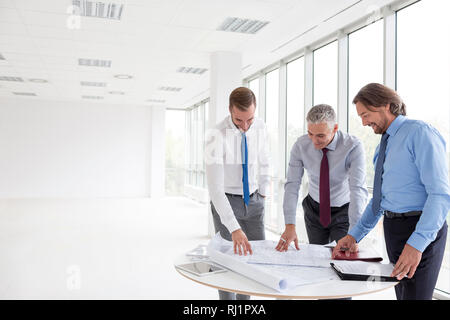 Colleghi di lavoro discutendo su blueprint a tavola nel nuovo ufficio Foto Stock