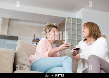 Allegro coppia amici con wineglasses seduti sul divano di casa Foto Stock