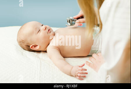 Un piccolo bambino, bambino, risiede nell'ufficio del medico e il medico ascolta i polmoni, il cuore. Il concetto di salute dei bambini Foto Stock