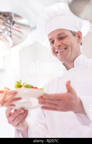 Lo chef sorridente dando piatto di insalata al cameriere in cucina al ristorante Foto Stock