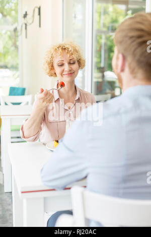 Sorridente donna bionda mangiare seduti con l uomo al tavolo nel ristorante Foto Stock