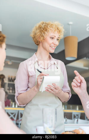 Sorridente cameriera facendo ordine da uomo seduto al ristorante Foto Stock