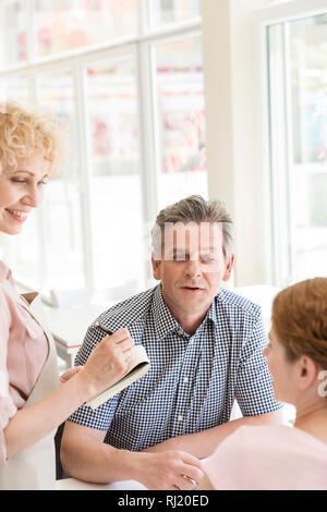 Sorridente cameriera di prendere ordini da clienti seduti al ristorante Foto Stock