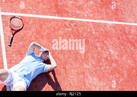 Elevato angolo di visione dei delusi uomo maturo con testa in mani mentre giaceva da racchetta da tennis su corte durante la stagione estiva Foto Stock
