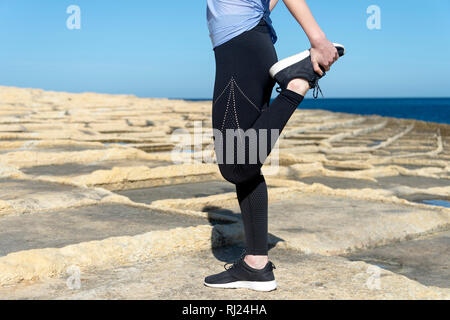 Closeupof una donna facendo il riscaldamento esercizi al di fuori nel sole, quad stretch. Foto Stock