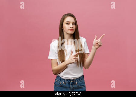 Primo piano della seria rigorosa giovane donna indossa una camicia bianca appare sottolineato e rivolta verso l'alto con un dito isolate su sfondo rosa Foto Stock