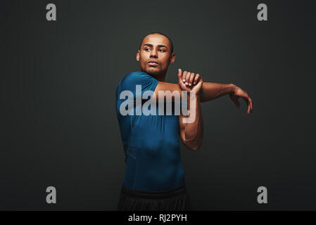 Ritratto di giovane forte uomo muscolare stretching le sue braccia. Africa Fitness modello maschile in piedi su sfondo scuro Foto Stock