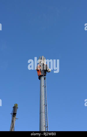 Due ingegneri di telecomunicazioni che lavorano in alto su palo di telefono cellulare con cielo blu a bury lancashire uk Foto Stock