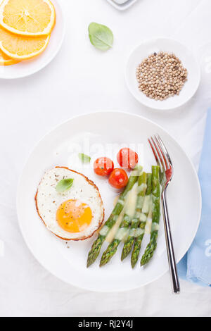 Uova fritte con asparagi e pomodori su una piastra bianca. Vista superiore Foto Stock