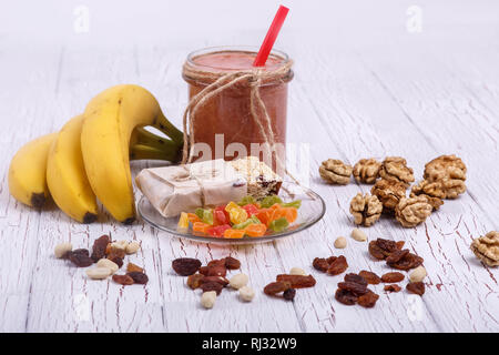 Red detox coctail con banane, di noci e frutta candita giace sul tavolo bianco Foto Stock