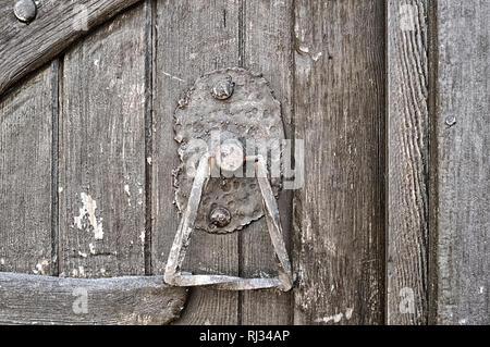 Ferro battuto maniglia della porta sul legno ruvido la vecchia porta fatta di tavole dipinte Foto Stock