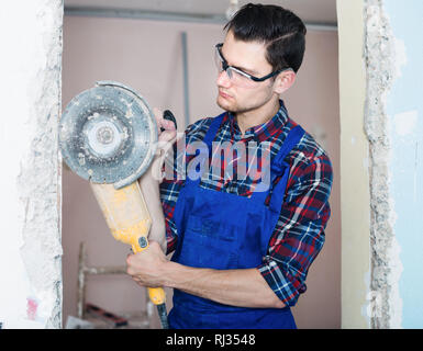 Giovane lavoratore utilizzando professional smerigliatrice angolare per parete di taglio Foto Stock