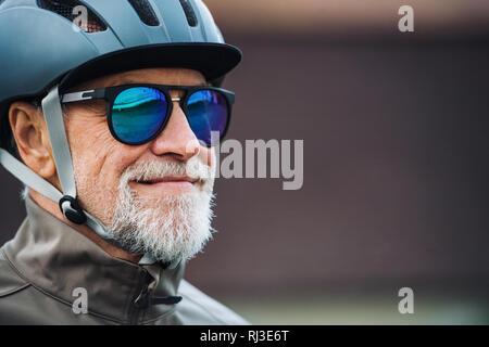 Close-up di active senior Uomo con occhiali da sole e casco in piedi all'esterno. Copia dello spazio. Foto Stock