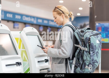 Casual donna caucasica utilizzando smart phone applicazione e check-in macchina all'aeroporto come ottenere la carta d'imbarco. Foto Stock