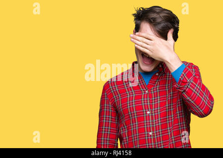 Giovane uomo bello con gli occhiali su sfondo isolato di sorridere e ridere con la mano sulla faccia che copre gli occhi per la sorpresa. Concetto di ciechi. Foto Stock