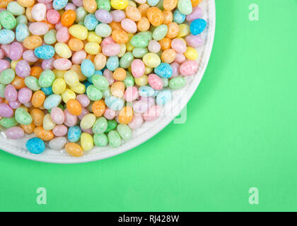 Molte colorate candy Jelly Beans sulla piastra di porcellana che posa in luce la superficie verde con copia spazio. Pasqua popolare candy. Foto Stock
