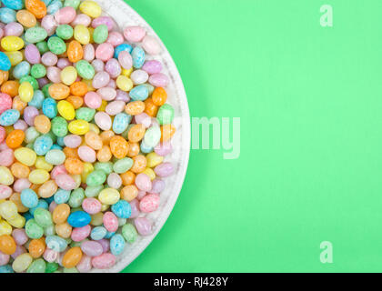 Molte colorate candy Jelly Beans sulla piastra di porcellana che posa in luce la superficie verde con copia spazio. Pasqua popolare candy. Foto Stock