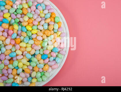 Molte colorate candy Jelly Beans sulla piastra di porcellana posa sulla luce rosa di superficie con copia spazio. Pasqua popolare candy. Foto Stock