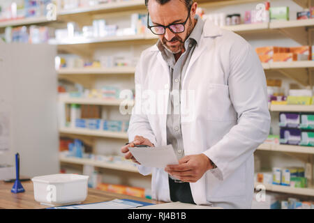 Il farmacista maschio prescrizione di lettura alla cassa. Maschio maturo farmacia lavora in un negozio di droghe. Foto Stock