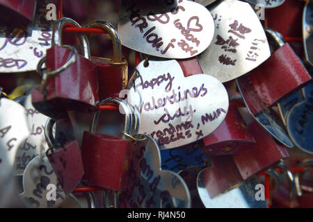 Liebesschlösser und beschriebene Herzen aus Metall hängen un einem roten Gestell Foto Stock