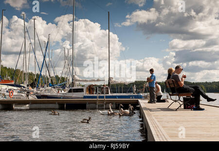 La famiglia dei cigni e barche ormeggiate a ponte al Lago Nidzkie, marina Pod Debem in Ruciane-Nida, la Masuria Lake District, Polonia, in Europa le persone sedute a essere Foto Stock