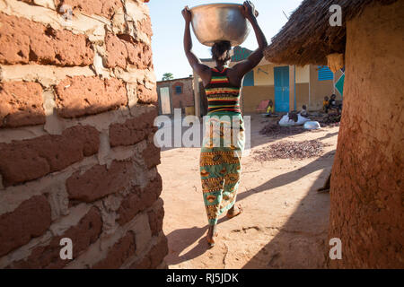 Bodadiougou Village, Banfora, Cascades Region, Burkina Faso, 4th dicembre 2016; una donna che ritorna al suo composto portando sulla testa un contenitore d'acqua. Foto Stock