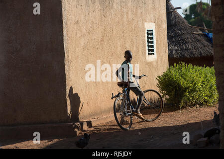 Bodadiougou Village, Banfora, Cascades Region, Burkina Faso, 4th dicembre 2016; un ragazzo in bicicletta attraverso il villaggio. Foto Stock