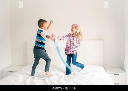 Due graziosi caucasica adorabili bambini divertenti di saltare sul letto in camera da letto e la riproduzione. Un ragazzo e una ragazza si diverte in combattimenti con palloncini. Migliori amici per Foto Stock