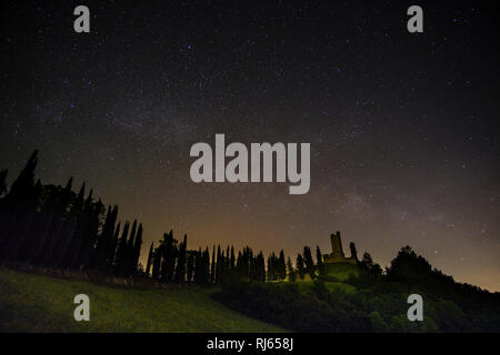 Tipico del territorio collinare della campagna toscana con campi e cipressi, Castello di Romena si trova sulla cima di una collina, di notte con la via lattea Foto Stock