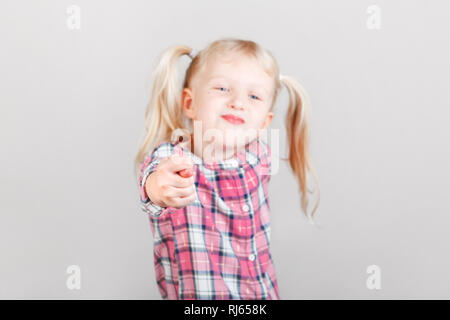 Carino adorabile bionda bianca caucasica ragazza in età prescolare rendendo volti nella parte anteriore della fotocamera. Bambino che mostra la fig segno e in posa di studio sulla pianura backgr luce Foto Stock