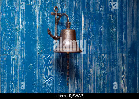 Il rame vecchia campana vintage, campanello, fune su un blu in legno invecchiato parete. Concetto di elemento di arredamento in interno del mazzo, cabina di nave, ristorante, sala, casa Foto Stock