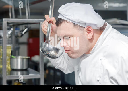 Closeup ritratto uomo chef professionale in bianco uniforme sta cercando piatto fatto fuori del mestolo. Concetto di controllo di qualità nel ristorante, il de Foto Stock