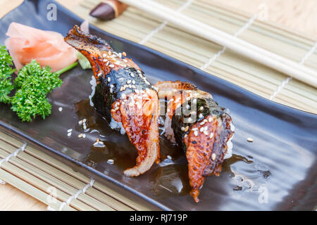 Il cibo giapponese Sushi Unagi è anguilla grigliate di pesce e riso per inumidire con salsa dolce in piastra nera su un tavolo di legno. Foto Stock