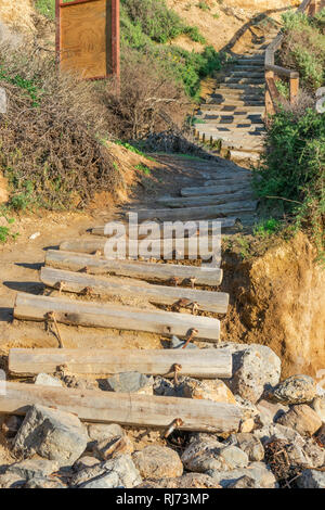 Vecchio weathered stair caso costituiti da tronchi di legno che conduce alla spiaggia, terminando sulle rocce Foto Stock