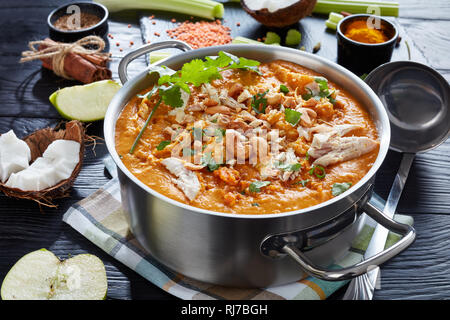 Sostanziosa piccante Mulligatawny minestra con carne di pollo cosparsi di anacardi fritti in una pentola di metallo su un tavoli in legno nero con ingredienti, Indiano e l'ENGL Foto Stock