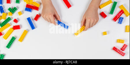 Kid le mani giocando con colorati la costruzione di mattoni di plastica su sfondo bianco. In via di sviluppo educativo sullo sfondo dei giocattoli Foto Stock