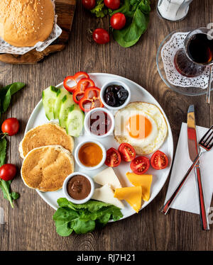 Enorme sana colazione spalmato su una tabella con caffè, tè, pomodoro, uova, pancake, marmellata e formaggio, Foto Stock