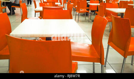 Svuotare il colore giallo sedie disposti in fila con il popolo sfocata sfondo nella hall. sala da pranzo con sedie di colore arancione, sfocata. Foto Stock