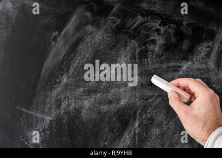 Mano che tiene il pezzo di gesso contro il vuoto lavagna polverosa Foto Stock