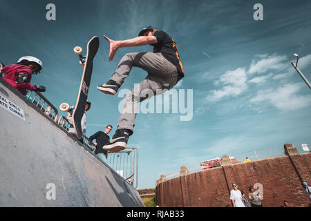 Un uomo pattinaggio salta fuori il suo skateboard e lo cattura dopo aver eseguito i trucchi sulla rampa ​a presso la laguna di Hove Skatepark, Hove, Brighton, Inghilterra. Foto Stock