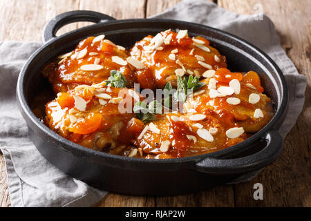 Stile rustico al forno cosce di pollo con albicocche secche e scaglie di mandorle close-up in una padella sul tavolo orizzontale. Foto Stock