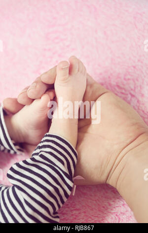 Adorabili poco Baby girl piedi detenute da papà su sfondo rosa Foto Stock