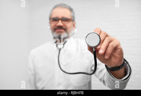 Il medico ORL azienda uno stetoscopio in mano, che lo mostra. In prossimità di apparecchiature mediche. Professional coppia terapista che indossa in bianco uniforme e bicchieri guardando la fotocamera e in posa. Foto Stock