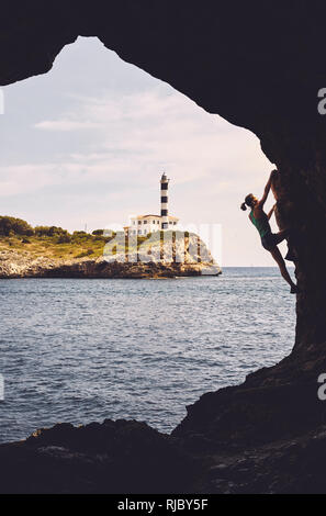 Silhouette di donna di arrampicata in una grotta, Portocolom faro in background, tonificazione del colore applicato, Mallorca, Spagna. Foto Stock