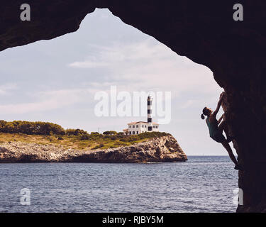 Silhouette di donna di arrampicata in una grotta, Portocolom faro in background, tonificazione del colore applicato, Mallorca, Spagna. Foto Stock