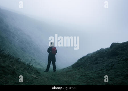 Un solitario escursionista incappucciato su un percorso in campagna cercando su un freddo spooky, nebbioso giorno. Foto Stock