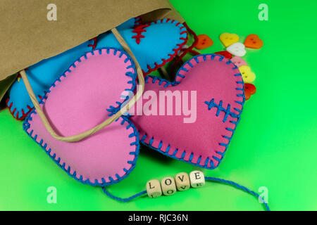 Sacchetto di carta pieno di cuore a mano souvenir e lettere di amore sul verde sfondo chroma key. Il giorno di San Valentino concetto Foto Stock