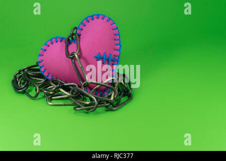 A forma di cuore gingillo giocattolo realizzato in gommapiuma rosa foglio e cuciti con fili blu, collegato ad una catena di metallo e sedersi sul chroma key superficie verde backg Foto Stock